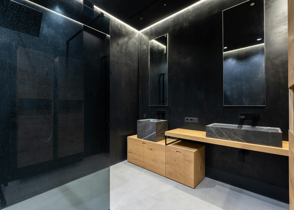 Interior of creative modern bathroom with shower cabin and mirrors hanging on black wall over marble sinks and wooden cabinets